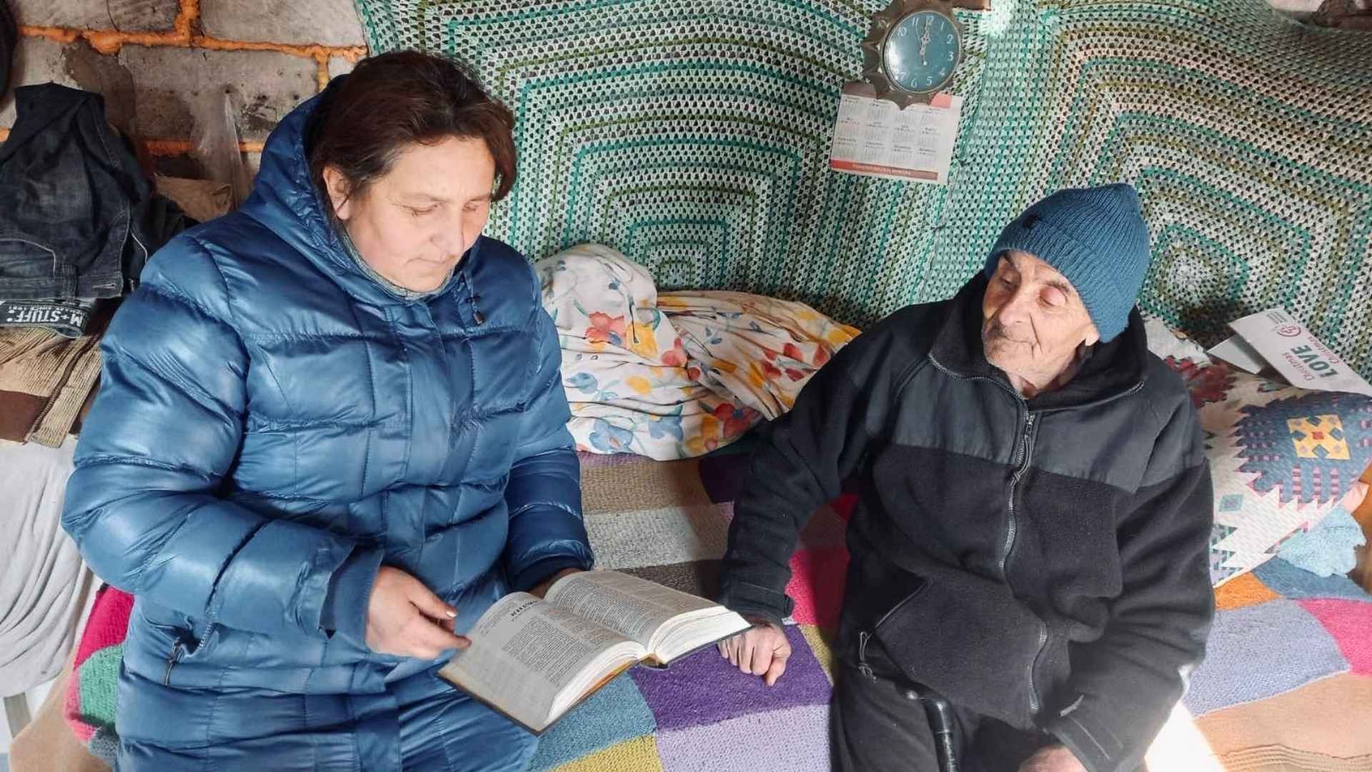 Woman and elderly man sitting on bed with a bible