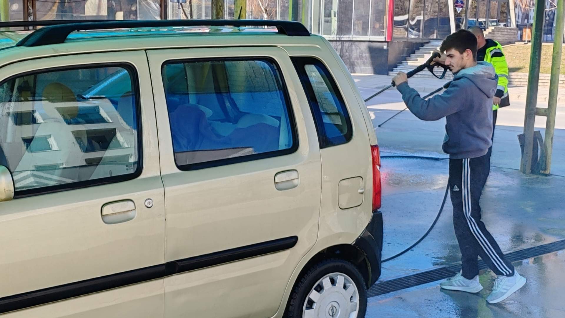 Young adult hosing down a vehicle at a carwash.