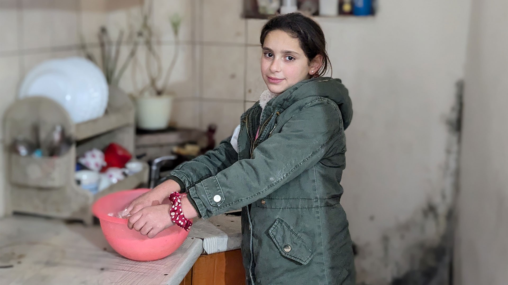 Girl in winter clothes kneading bread dough in a pink bowl.