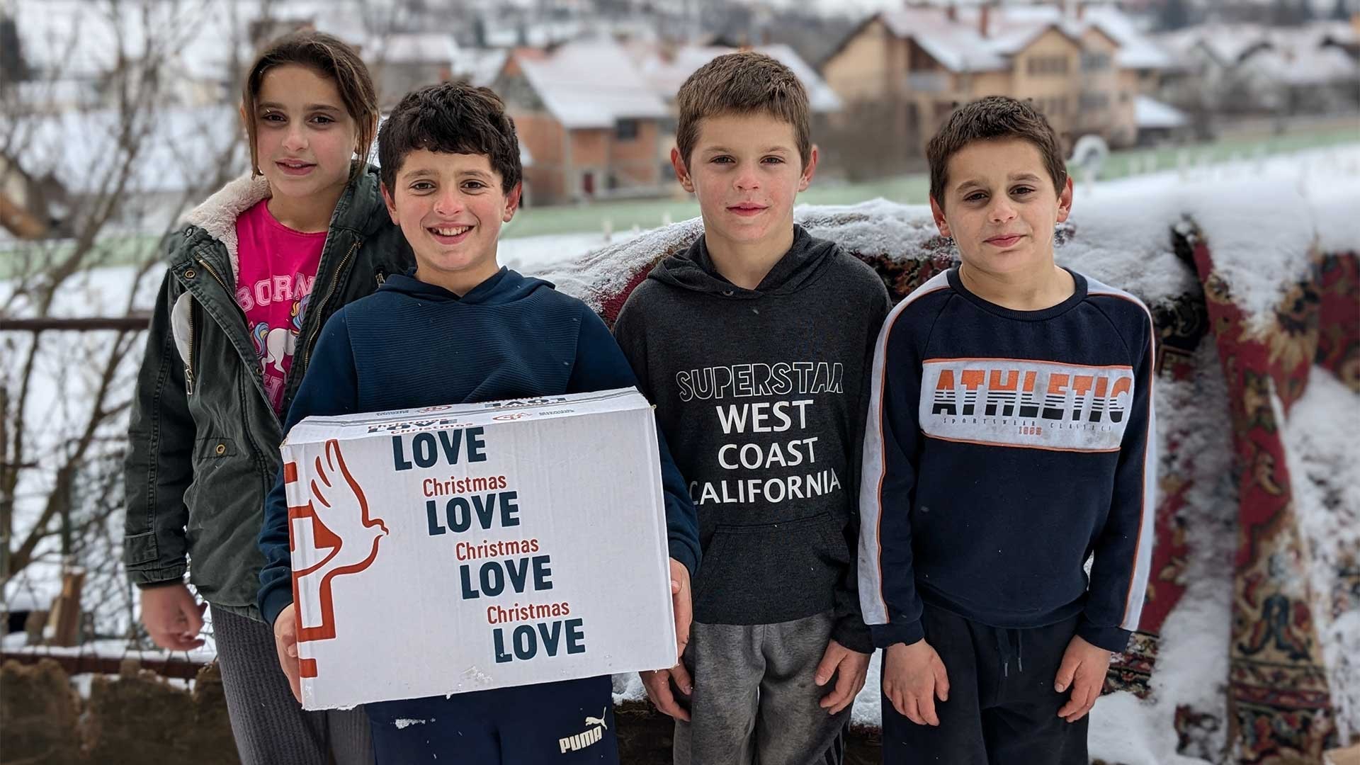 A girl and three boys standing in the snow, with one boy holding a box.