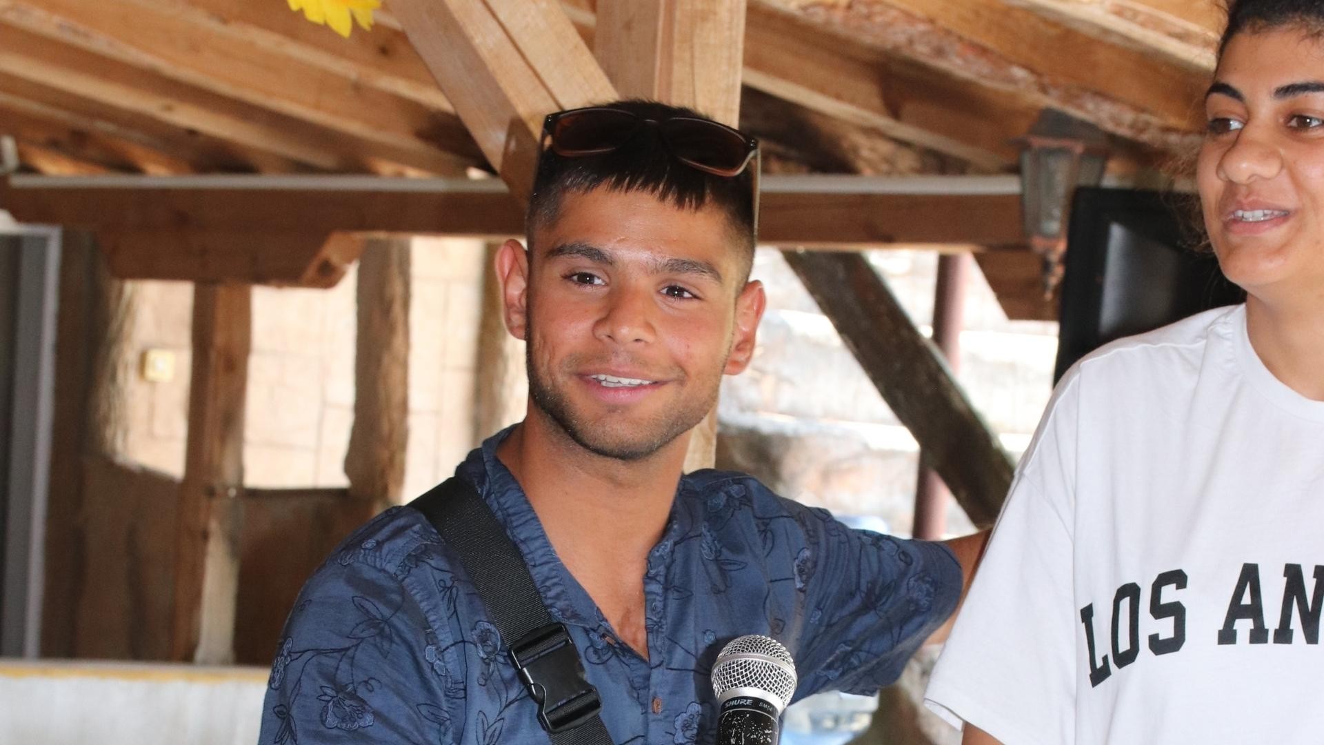 Young man with a warm smile holding a microphone, standing beside a young woman.