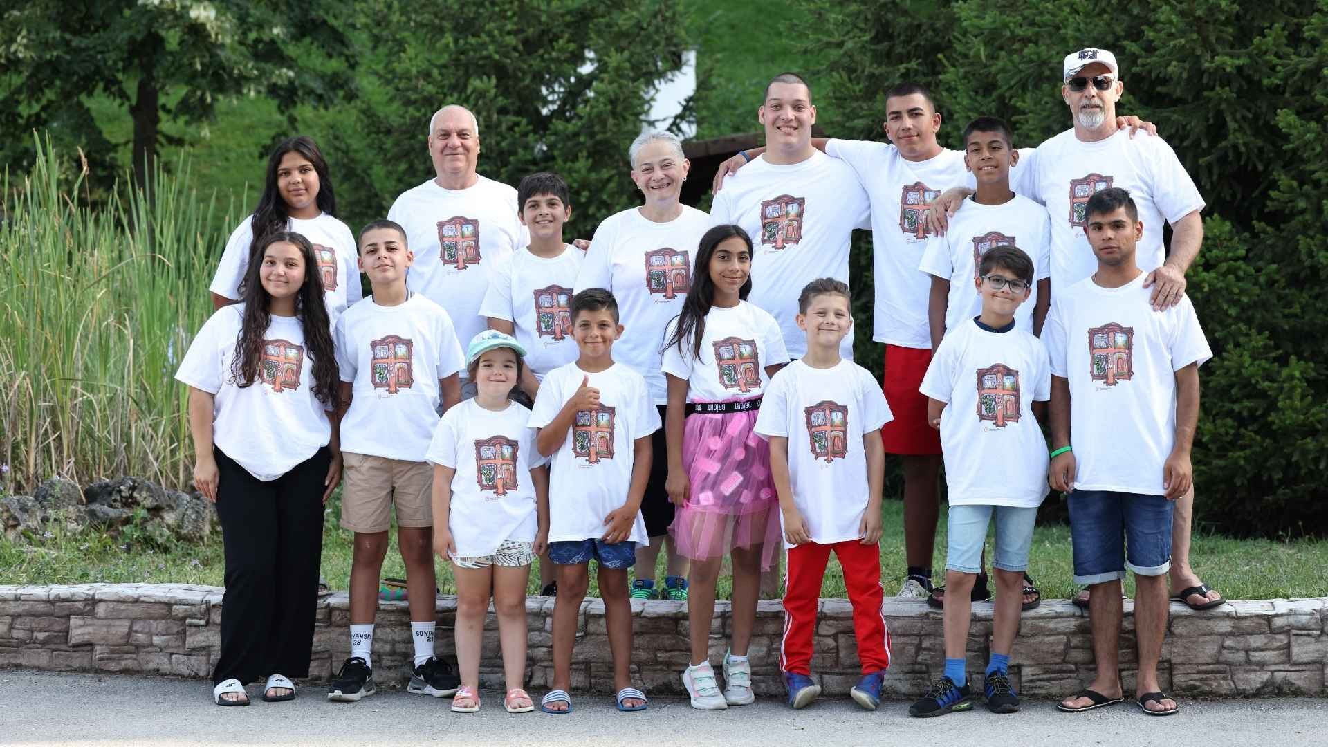 Group of smiling children and adults wearing matching t-shirts, standing together outdoors.