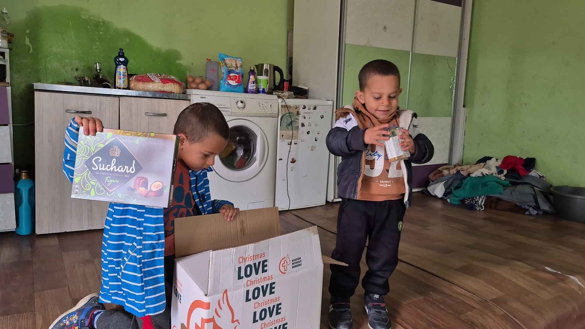 Two children unpacking the contents of a Christmas food box indoors.